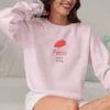 Close-up of a model wearing a Light Pink crewneck sweatshirt showing the detail of the Paris beret graphic.