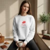 Model wearing a White sweatshirt with a red beret design sitting by a sunny window with coffee and a croissant.