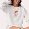 Close-up of a model wearing a White crewneck sweatshirt showing the detail of the Paris beret graphic.