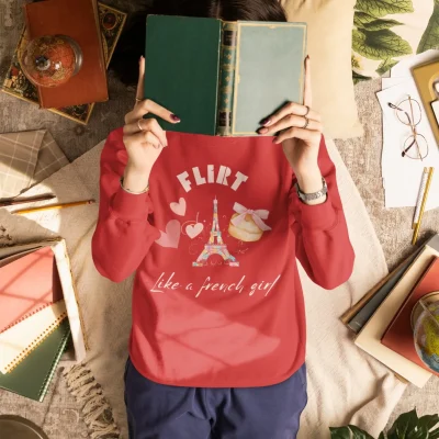 Woman in a cozy red sweatshirt with French macaron and Eiffel Tower design, reading a book in a soft, romantic setting — Bhoomkins soft girl aesthetic.